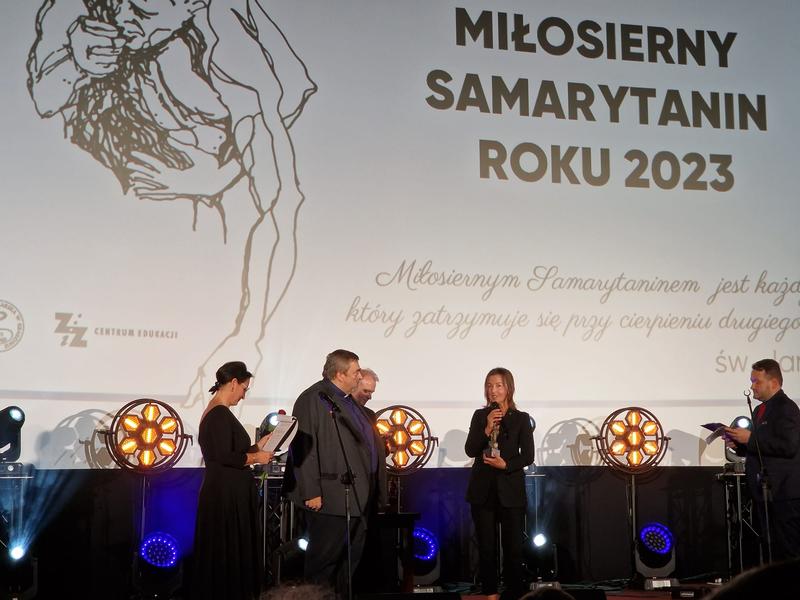 Katarzyna Jachymska stoi na scenie i odbiera nagrodę Miłosierny Samarytanin.