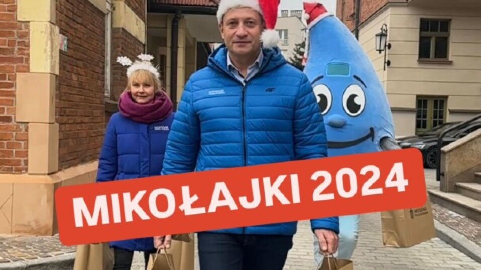 Trzy osoby przebrane za Mikołaja, śnieżynkę i kroplę wody w stroju mikołajkowym niosą prezenty.