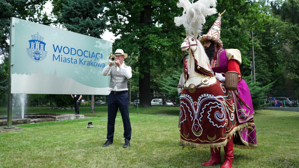 Lajkonik i trębacz w tle tablica z napisem Wodociągi Miasta Krakowa