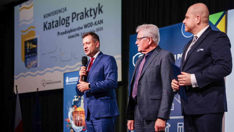 Na scenie trzech mężczyzn w&nbsp;garniturach przemawia do&nbsp;publiczności