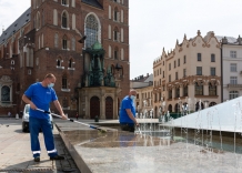 Dwóch pracowników wodociągów czyści fonannę na Rynku Głównym w tle widać Kościół Mariacki.