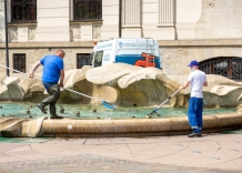 Dwóch pracowników wykonuje prace porządkowe przy fontannie na pl. Szczepańskim