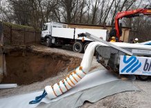 Montaż instalacji kanalizacyjnej - długi rękaw wpuszczany pod ziemię. W tle samochód specjalistyczny.