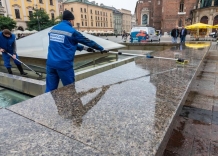 Dwóch pracowników Wodociągów Miasta Krakowa czyści fontannę na Rynku Głównym.