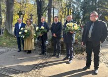 Przedstawiciele Zarządu Wodociągów Miasta Krakowa stoją nad grobem trzymając wiązanki kwiatów