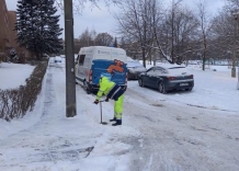 Na zaśnieżonej ulicy pracownik wodociągów odkręca właz specjalnym narzędziem.